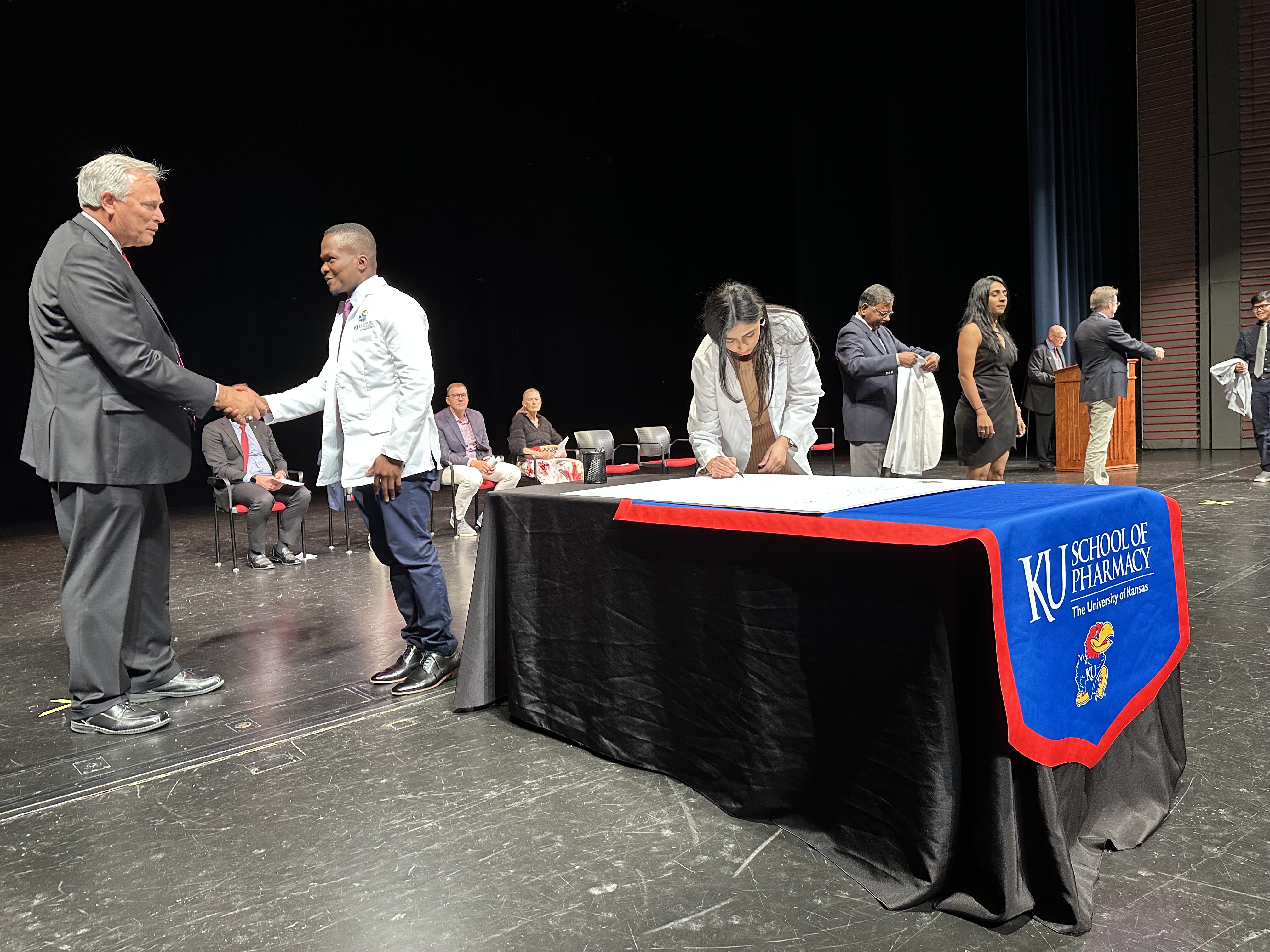 Dean Ronald Ragan congratulates P1 student Kossivi Abalo while student Haya Abbas signs the Pledge of Professionalism at the school's 2023 white coat ceremony.