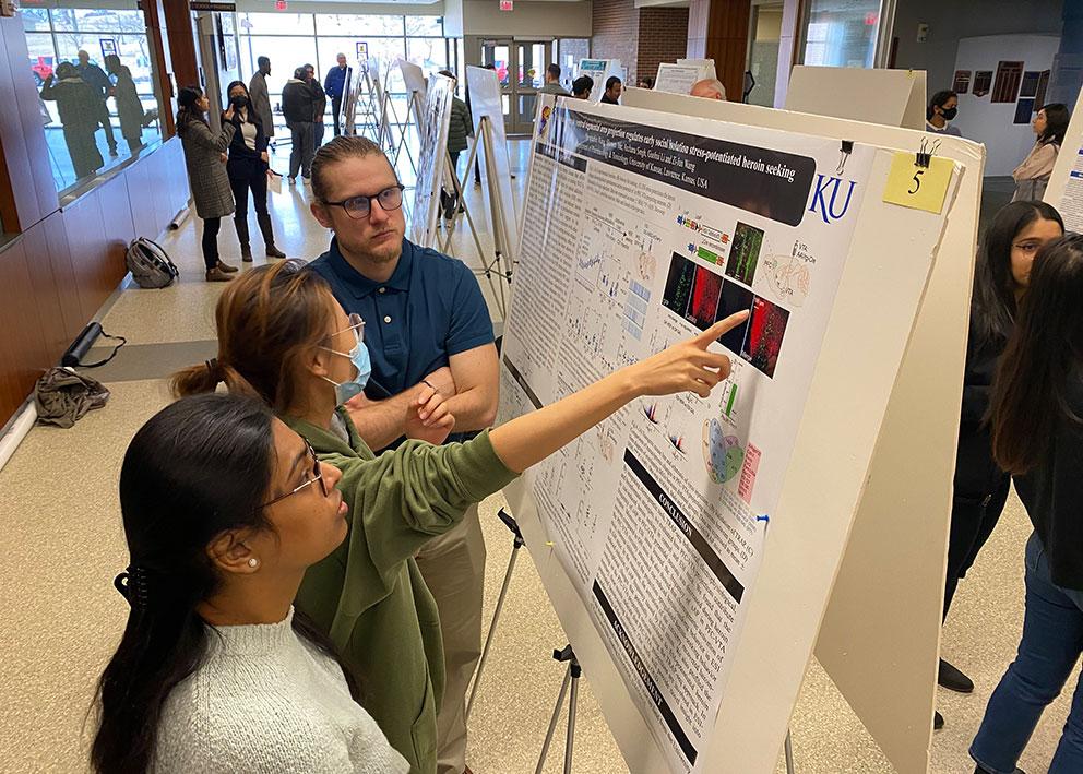 KU Pharmacy student points at graphic on research poster while two other students look on
