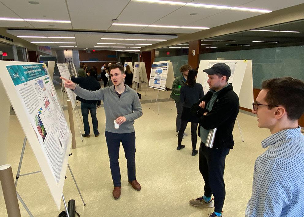 Two KU Pharmacy students look on as another student points to research poster